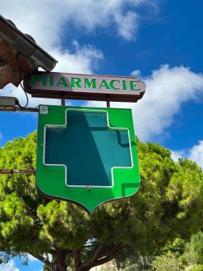 Mavi gökyüzü ve çam ağaçlarına karşı eczane işareti. Yakın plan. Saint-Paul-de-Vence. Fransa.