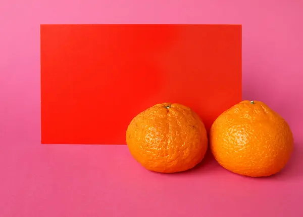 Two tangerines and a red rectangle for an inscription on a pink background