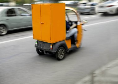 Görüntü. Üç tekerlekli scooterlı bir kurye mal teslimatı için emir verir..