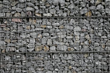 Dağların parçalanmasını önlemek için metal bir ızgaranın arkasındaki küçük gri taşlardan yapılmış bir duvar. Taş dokusu