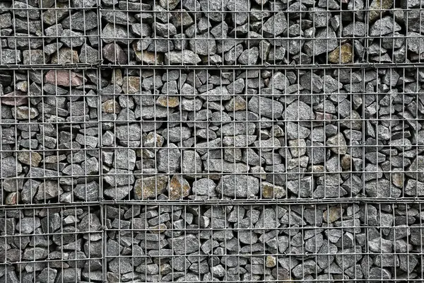 Dağların parçalanmasını önlemek için metal bir ızgaranın arkasındaki küçük gri taşlardan yapılmış bir duvar. Taş dokusu