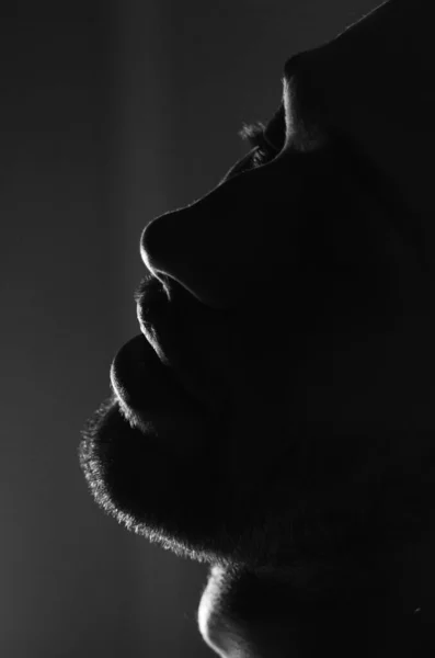 Silhouette of a male unshaven face. Lips, nose, eyes. Monochrome photo. Young male profile portrait