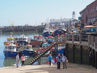 Scarborough, Kuzey Yorkshire, İngiltere - 11 Eylül 2022: Scarborough limanındaki balıkçı tekneleri ve balıkçı tekneleri önünde liman binaları olan turistler