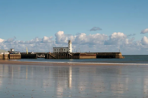 stock image scarborough lighthouse and harbour reflected on the south bay beach in summer sunshine