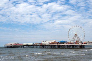 Blackpool, Lancashire, United Kingdom - 27 July 2024 : Blackpool central pier with ferris wheel and rides with the sea at high tide in summer sunlight clipart