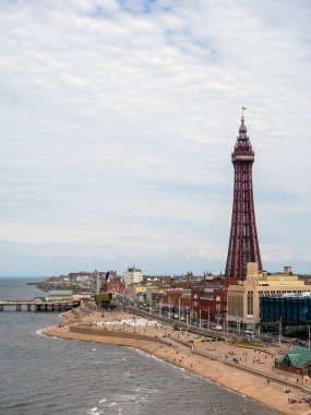 Blackpool, Lancashire, Birleşik Krallık - 27 Temmuz 2024: Gezinti güvertesi boyunca binalar ve plaj insanları tarafından çevrili Blackpool kulesi
