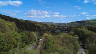 Hava aracı görüntüsü, batı Yorkshire 'daki Mytholmroyd köyüne doğru bakıyor. Yol ve çevresindeki tepeler ve ağaçlar arasında binalar görünüyor.