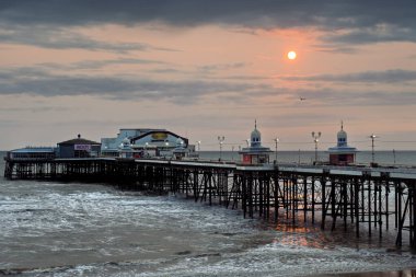 Blackpool Kuzey İskelesi, gün batımında. Kızıl dramatik bir gökyüzü, yaklaşan gelgitle denize yansıyor.