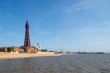 Denizden Blackpool 'un panoramik manzarası yaz güneşinde merkez rıhtımı olan kuleyi ve deniz kenarındaki binaları gösteriyor.
