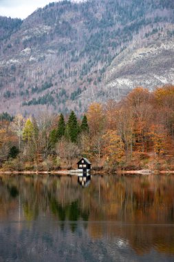 Bohinj Gölü 'nde sonbahar yansımaları ve ön planda bir kır evi.