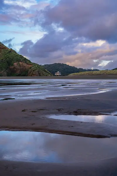 Reflective sunset moment at the beautiful Bethells surf beach, Auckland, New Zealand