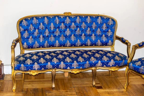 blue and gold sofa against a white wall and brown floor