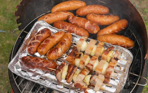 在家庭便携式烤架上烤香肠 熏肉和洋葱 — 图库照片