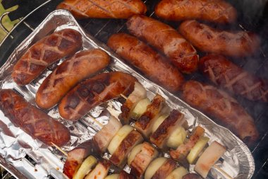 Ev portatif ızgarada ızgara sosis, pastırma ve soğan.