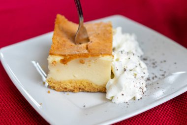 Krem şantili cheesecake beyaz tabakta ve kırmızı arka planda