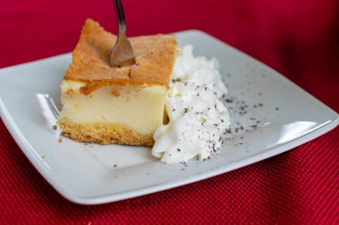 Krem şantili cheesecake beyaz tabakta ve kırmızı arka planda