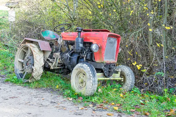Eski bir kırmızı çiftlik traktörü ormanın arka planında