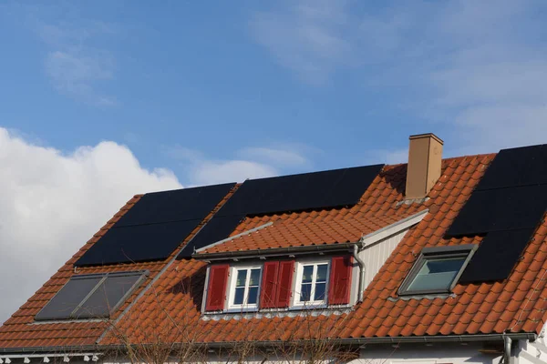 A residential building roof with dormer and skylights. Modern solar modules are laid on the tiled roof and provide for their own power generation