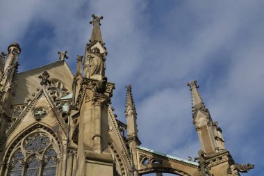 View of the top of the Johannes Church in Stuttgart. The fictitious roof landscape with spiers, decorations and statues is reminiscent of an impressive cathedral. The bright sandstone shines in the spring sun and the blue sky with light clouds makes 