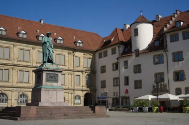 Stuttgart 'taki Schiller Meydanı. Friedrich Schiller anıtı kaldırım taşı meydanının üzerindeki bir kaideye yükseliyor. Heykelin arkasında Prens 'in Mağarası var. Sağında Parazoyla korunan bir restoran terası olan Eski Başbakanlık binası var.