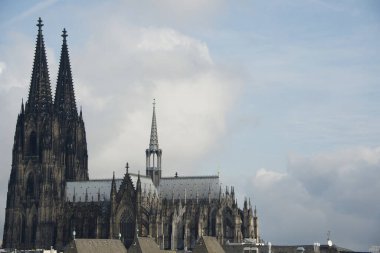 The Cologne Cathedral with its high towers in the overall view. The cathedral towers over all the residential roofs in the neighborhood. But compared to the gigantic mountains of clouds in the sky, the Gothic structure seems almost small clipart