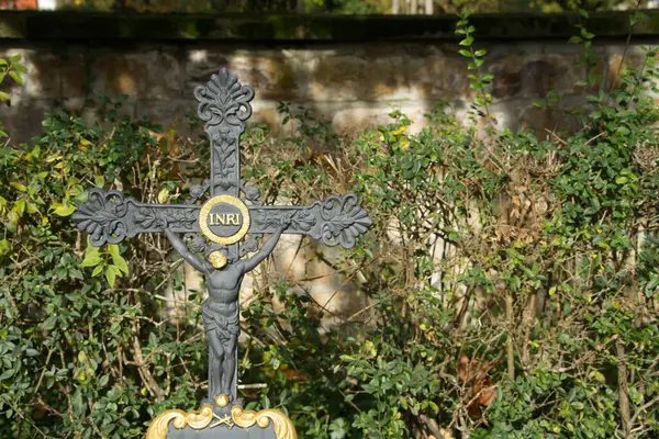 An ancient grave cross made of iron with ever-gilded details. The INRI inscription was gilded and also covered with gold leaf to emphasize the wreath. The shield below the crucified figure is also framed with gold leaf. Jesus\' face also shines gilded