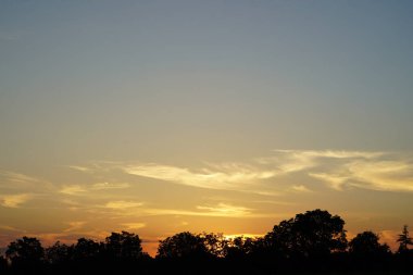 Güneş eski ceviz ağaçlarının arkasında batıyor ve gökyüzü muhteşem bir şekilde renk değiştiriyor.