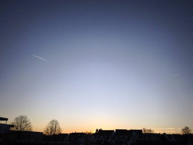 Açık bir kış günü. Kasabanın kıyısındaki evlerin arkasında güneş ufukta batıyor. Küçük evler ve uzun ağaçlar siluet olarak görülebilir. Gökyüzünde, güneşin aydınlattığı iki zıt zıt zıt zıt ışık var..