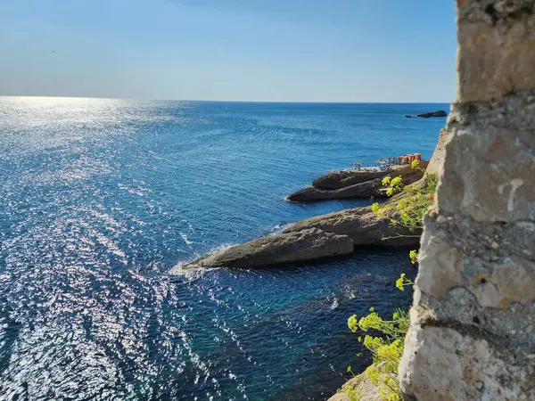 Güneşli bir günde mavi deniz kıyısında kayalar.