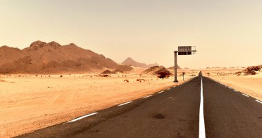 Sahra Çölü 'nde yol, uzun düz asfalt yolu, turuncu kum ve etrafındaki dağlar. 
