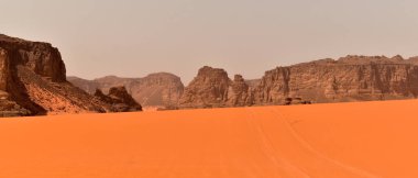 Tadrart Rouge 'da kaya oluşumları, Tassili N' Ajjer Ulusal Parkı. Sahra Çölü, turuncu kum ve kayalar. Kumda araba izi var. Tatiller ve Cezayir 'de seyahat. Sahra, Cezayir, Afrika.