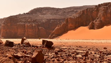 Tadrart Rouge 'da kaya oluşumları, Tassili N' Ajjer Ulusal Parkı. Sahra Çölü, turuncu kum ve kayalar. Arka planda iki cesur bisikletçi çölde. Tatiller ve Cezayir 'de seyahat. Sahra, Cezayir, Afrika.