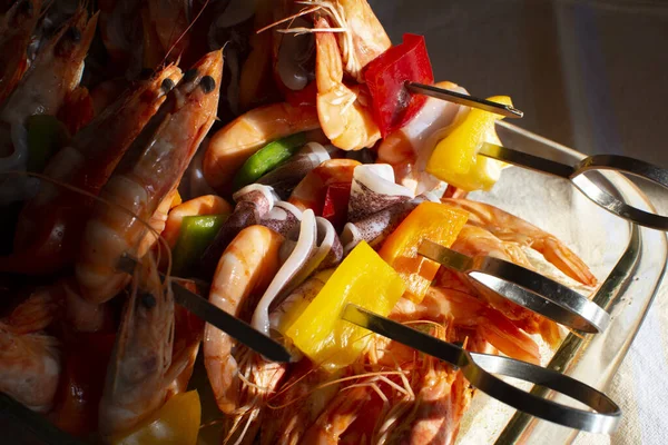 Ananas parçaları ve ızgara için hazırlanmış renkli biberli metal şişler üzerine yerleştirilmiş karides kebabı.