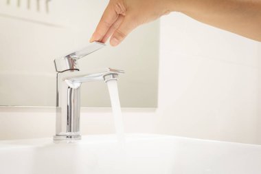 Kadın açık, krom musluk lavabosunu çek ve su musluğundaki corona virüsü için el sabunu yıka. Akan suyu itin. Lavabo lavabosunun musluğu olan banyo içi arka plan.