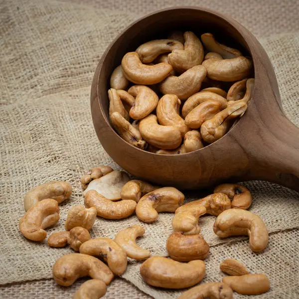 Roasted cashew nuts and halves in wooden bowl on table top view. Macro studio shot Homemade Roasted Salted Cashews in basket and spoon breakfast on sack, Healthy food Seeds snack product