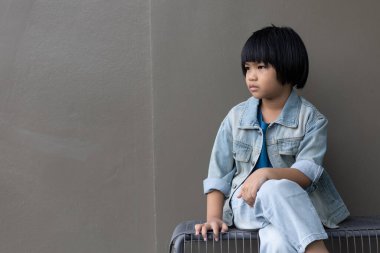 Kot pantolon giymiş bir kız çocuğu stüdyosunda arkadaşıyla dikiliyor. Ailesinin evindeki gri duvarlara bakan üzgün bir kız.