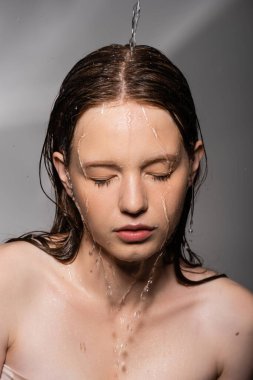 Water pouring on hair and face of young model on grey background  clipart