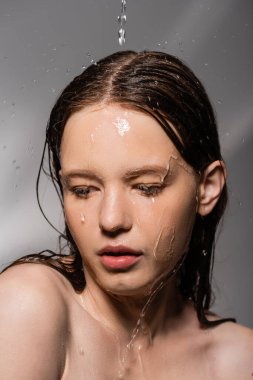 Young woman with naked shoulders standing under water pouring on grey background  clipart