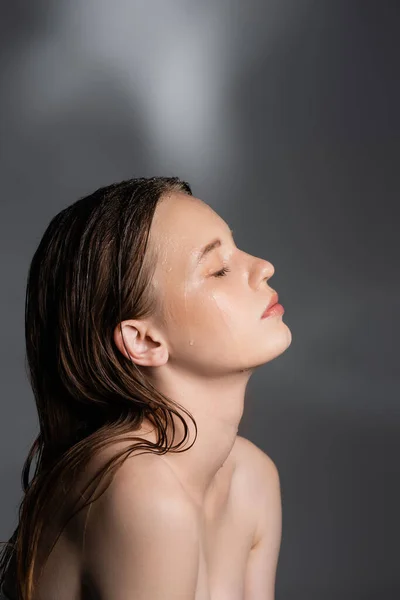 灰色の背景に濡れた髪と肌を持つ若いモデルの側面図 — ストック写真