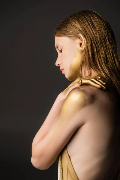 Side view of woman with makeup and golden paint on skin isolated on grey