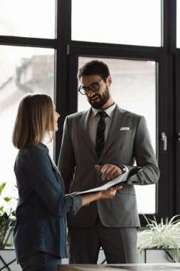 Gülümseyen işadamı, ofisteki genç iş arayanın yakınındaki özgeçmişine işaret ediyor 