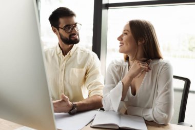 Ofisteki bilgisayar ve defterin yanında yöneticiye bakan neşeli yeni işçi. 