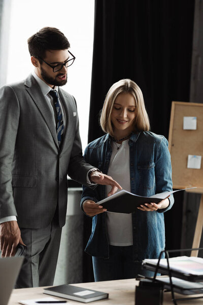 Бизнесмен в костюме указывает на резюме рядом с улыбающейся женщиной в офисе 