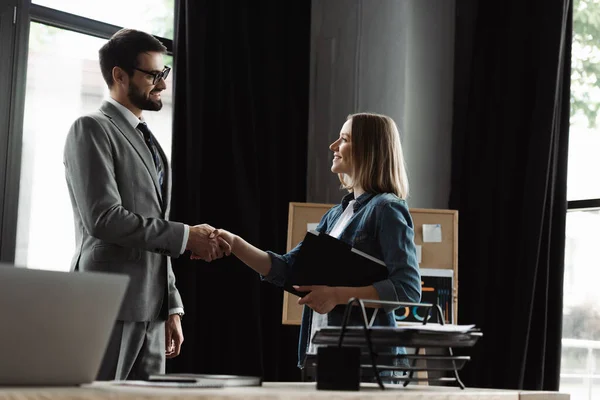 オフィスでの面接中に履歴書を持っている笑顔の女性とビジネスマンと握手 — ストック写真