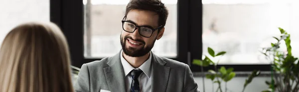 stock image Cheerful businessman in suit looking at blurred woman on job interview in office, banner 