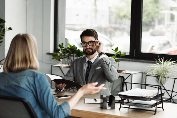 Менеджер в очках и костюмах, держащий бумажную папку с резюме и глядя на кандидата в президенты 