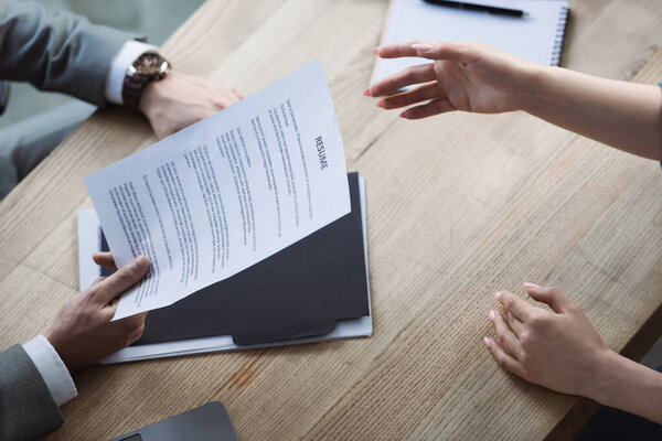 Высокий угол зрения женщины указывая рукой рядом с бизнесменом холдинг резюме во время собеседования 