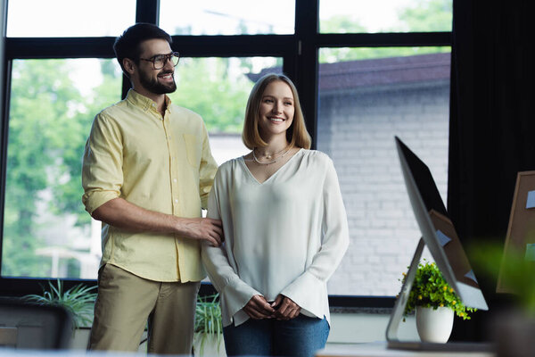 Smiling manager standing near young colleague on internship in office 