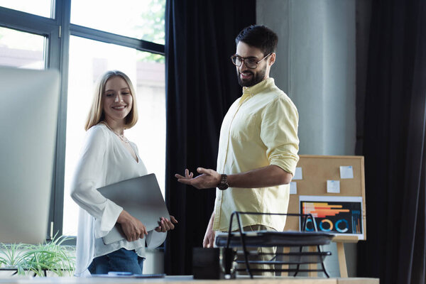 Позитивный бизнесмен разговаривает с коллегой с ноутбуком во время стажировки в офисе 