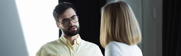 Businessman in eyeglasses talking to blurred intern in office, banner